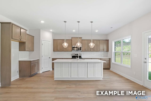 kitchen with a center island with sink, light hardwood / wood-style flooring, decorative light fixtures, and sink