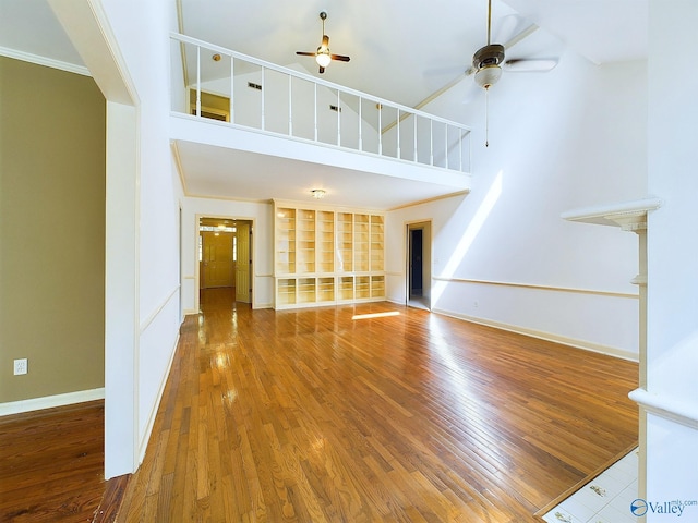 unfurnished living room featuring hardwood / wood-style flooring, ceiling fan, crown molding, and a high ceiling