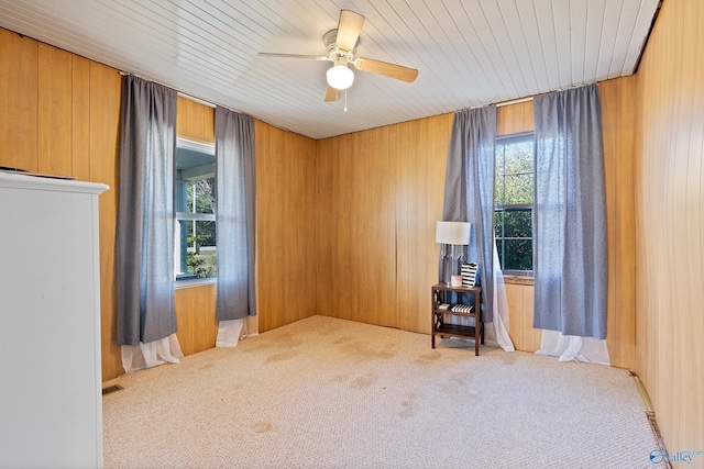 spare room featuring wood walls, ceiling fan, a healthy amount of sunlight, and light colored carpet