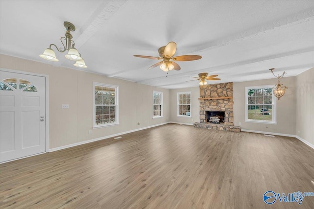 unfurnished living room featuring ceiling fan with notable chandelier, a stone fireplace, wood finished floors, and baseboards