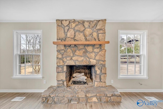 details with ornamental molding, visible vents, a stone fireplace, and wood finished floors