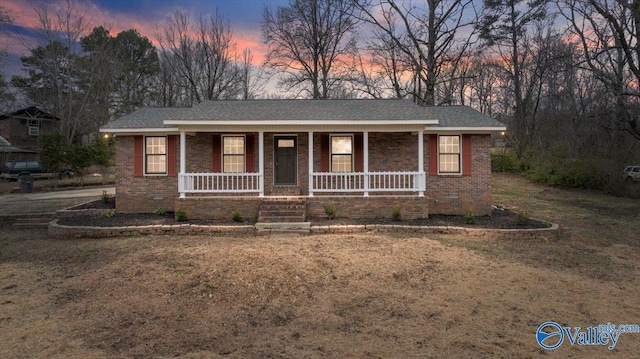 ranch-style home featuring covered porch, roof with shingles, brick siding, and a lawn