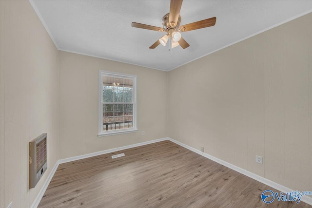 unfurnished room featuring baseboards, visible vents, light wood-style flooring, heating unit, and crown molding