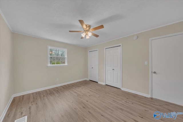 unfurnished bedroom featuring visible vents, a ceiling fan, a textured ceiling, light wood-type flooring, and two closets