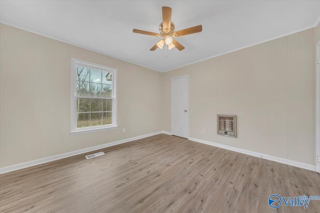 empty room featuring ceiling fan, visible vents, baseboards, light wood-style floors, and heating unit