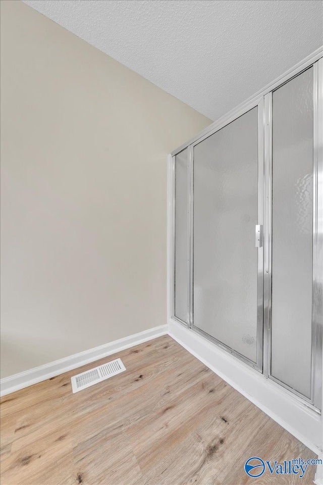 full bath with visible vents, a textured ceiling, baseboards, and wood finished floors