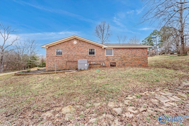view of side of home featuring cooling unit, brick siding, and a lawn