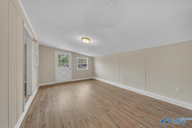 interior space featuring light wood-style floors, vaulted ceiling, a textured ceiling, and baseboards