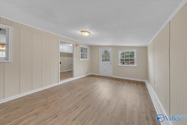 unfurnished room with a textured ceiling, baseboards, light wood-style flooring, and crown molding