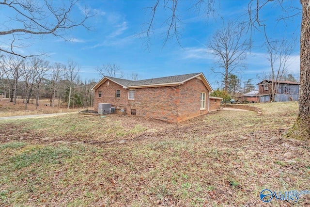 view of side of home featuring crawl space, brick siding, a lawn, and central AC unit