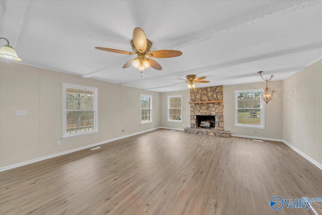 unfurnished living room with beamed ceiling, a fireplace, wood finished floors, and a wealth of natural light