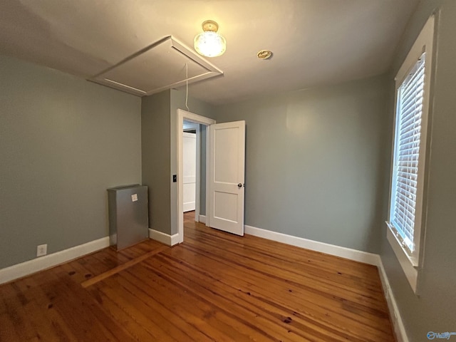 spare room with attic access, plenty of natural light, baseboards, and wood finished floors