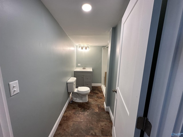 bathroom with a shower, toilet, stone finish flooring, vanity, and baseboards