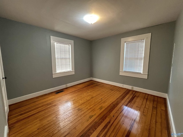 unfurnished room featuring baseboards, visible vents, and wood-type flooring