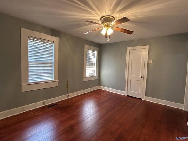 empty room featuring a ceiling fan, visible vents, dark wood finished floors, and baseboards