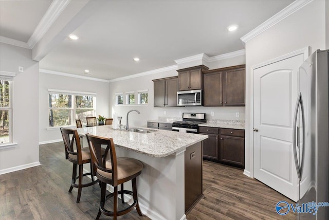 kitchen with stainless steel appliances, dark wood-type flooring, sink, an island with sink, and light stone countertops