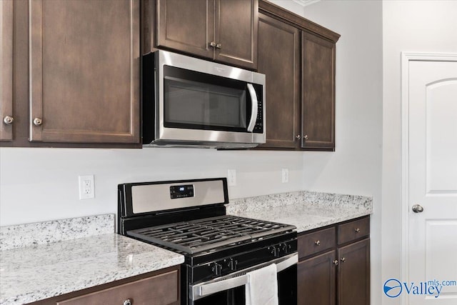 kitchen with stainless steel appliances, light stone countertops, and dark brown cabinetry