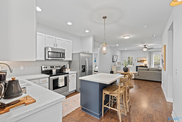 kitchen with white cabinetry, appliances with stainless steel finishes, decorative light fixtures, dark hardwood / wood-style floors, and a kitchen breakfast bar