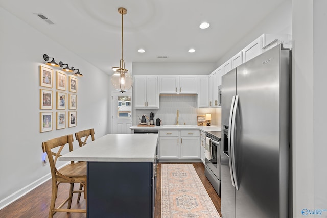 kitchen with wood-type flooring, a kitchen island, appliances with stainless steel finishes, a breakfast bar, and white cabinets