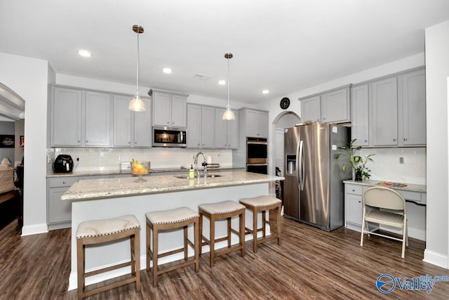 kitchen with appliances with stainless steel finishes, a kitchen island with sink, hanging light fixtures, and a sink