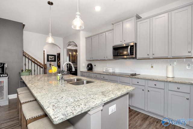 kitchen featuring arched walkways, stainless steel microwave, a sink, and a center island with sink