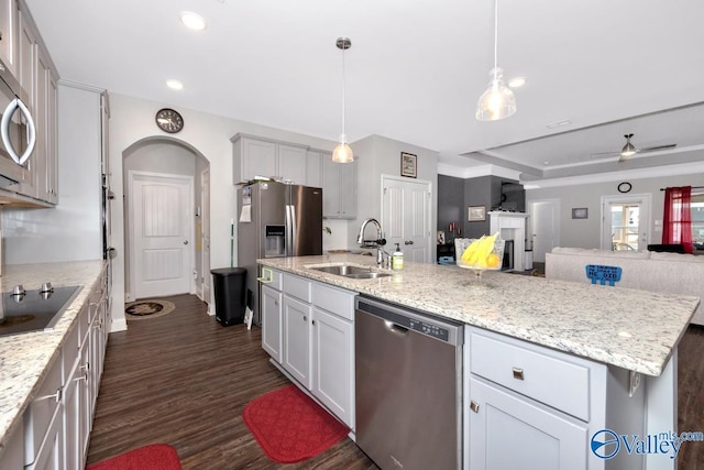 kitchen featuring arched walkways, pendant lighting, a center island with sink, stainless steel appliances, and a sink