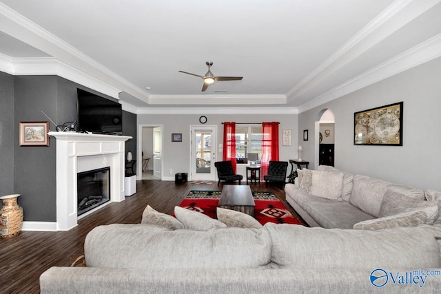 living area featuring arched walkways, a fireplace, a raised ceiling, dark wood-type flooring, and baseboards