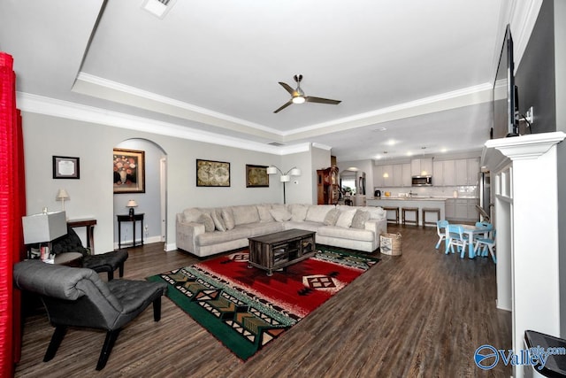 living room with arched walkways, visible vents, dark wood finished floors, a raised ceiling, and crown molding