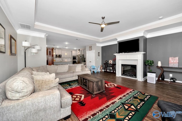 living room with ceiling fan, wood finished floors, visible vents, a glass covered fireplace, and crown molding