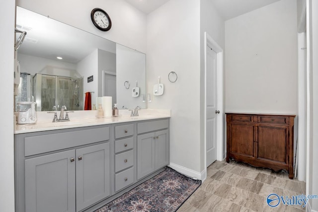 bathroom featuring double vanity, a shower stall, baseboards, and a sink