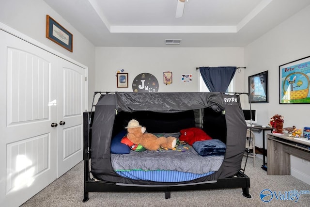 bedroom with ceiling fan, a tray ceiling, visible vents, and light colored carpet