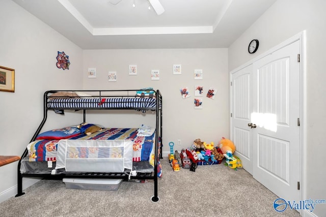 carpeted bedroom featuring baseboards, a raised ceiling, and a ceiling fan