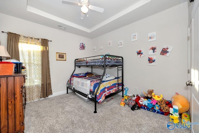 carpeted bedroom featuring a ceiling fan, a raised ceiling, visible vents, and baseboards