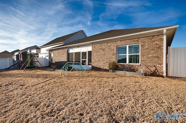 back of property featuring fence, a lawn, and brick siding