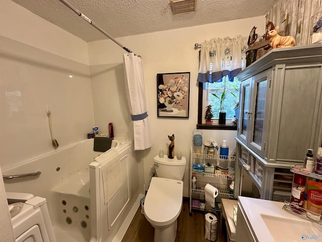 bathroom featuring a textured ceiling, toilet, vanity, washer and dryer, and hardwood / wood-style flooring