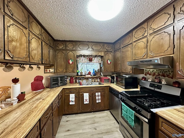 kitchen featuring butcher block counters, sink, stainless steel appliances, a textured ceiling, and light wood-type flooring