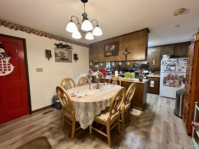 dining room with a textured ceiling, a notable chandelier, and light wood-type flooring