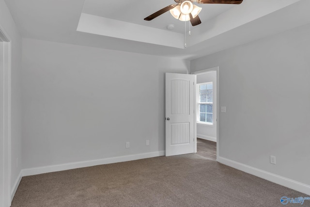 empty room featuring a tray ceiling, carpet flooring, a ceiling fan, and baseboards