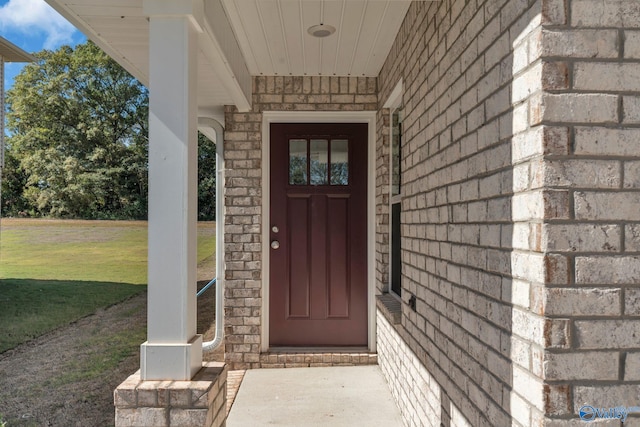 view of exterior entry with a lawn and brick siding