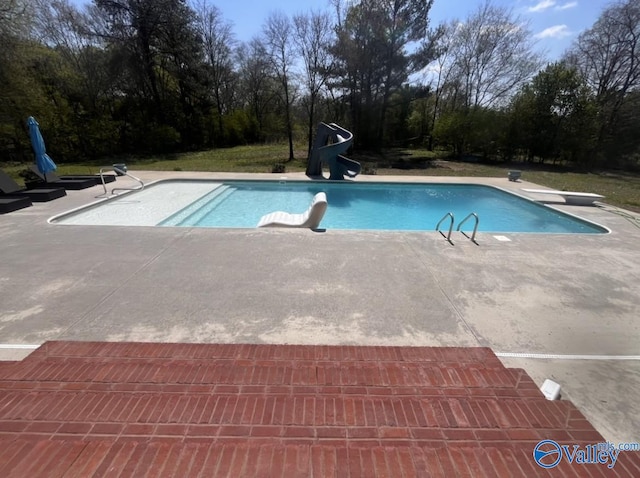 view of swimming pool with a water slide, a diving board, and a patio area