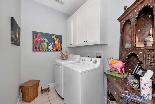 clothes washing area featuring cabinets, light tile patterned floors, washing machine and clothes dryer, and a textured ceiling