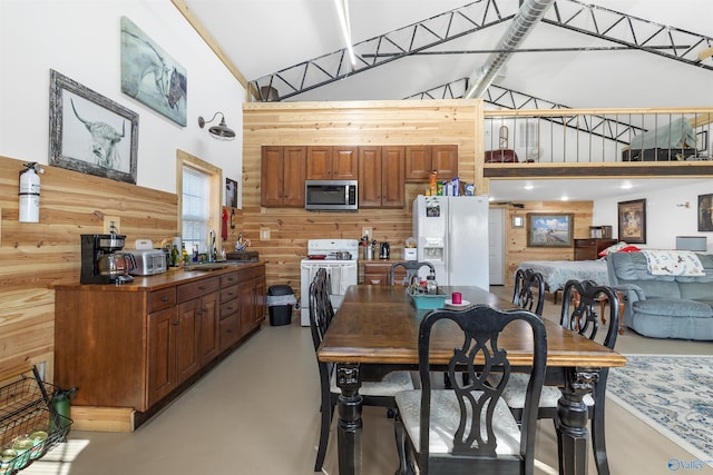 dining area with sink, high vaulted ceiling, and wood walls