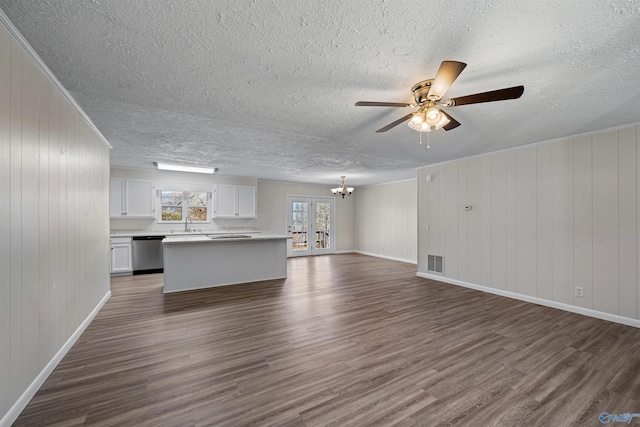 unfurnished living room with ceiling fan with notable chandelier, dark hardwood / wood-style flooring, wooden walls, and french doors