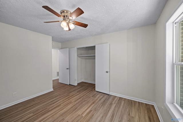 unfurnished bedroom with ceiling fan, a closet, a textured ceiling, and light wood-type flooring