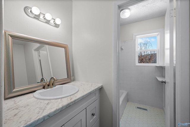 bathroom featuring a textured ceiling, vanity, and tiled shower / bath combo