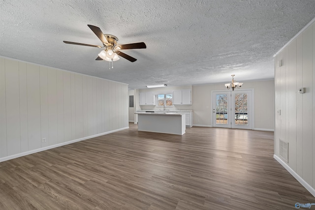 unfurnished living room featuring ceiling fan with notable chandelier, sink, dark wood-type flooring, and wooden walls