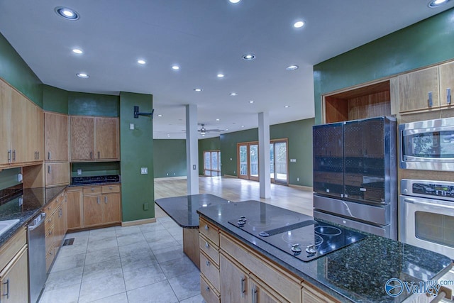 kitchen featuring ceiling fan, stainless steel appliances, light tile patterned floors, and dark stone countertops