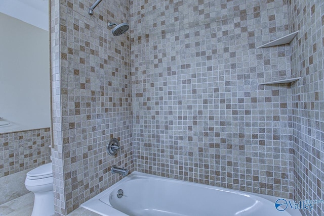 bathroom with tile walls, tiled shower / bath, and toilet