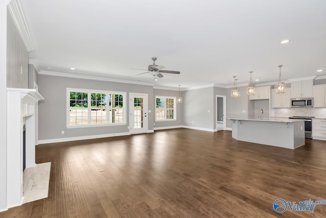 unfurnished living room featuring ceiling fan with notable chandelier, crown molding, sink, and dark hardwood / wood-style flooring