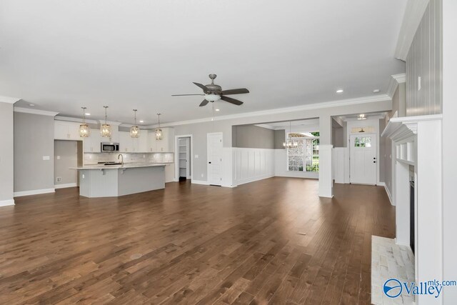 unfurnished living room with ceiling fan with notable chandelier, dark hardwood / wood-style floors, and crown molding